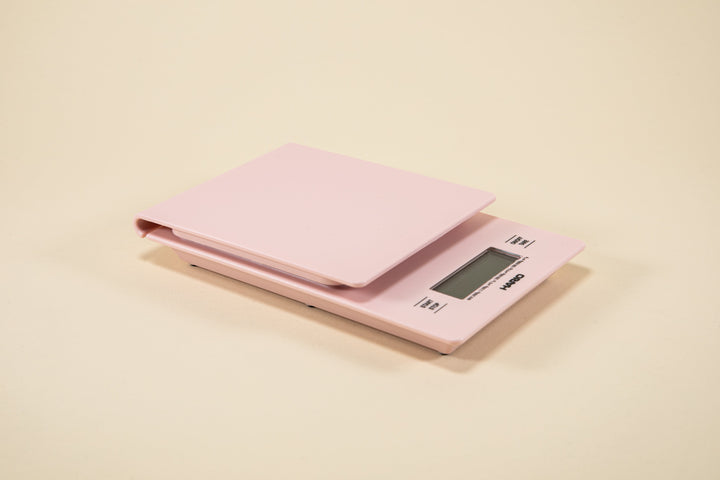 A matte pink V60 Drip Scale with a digital display, placed on a plain surface.