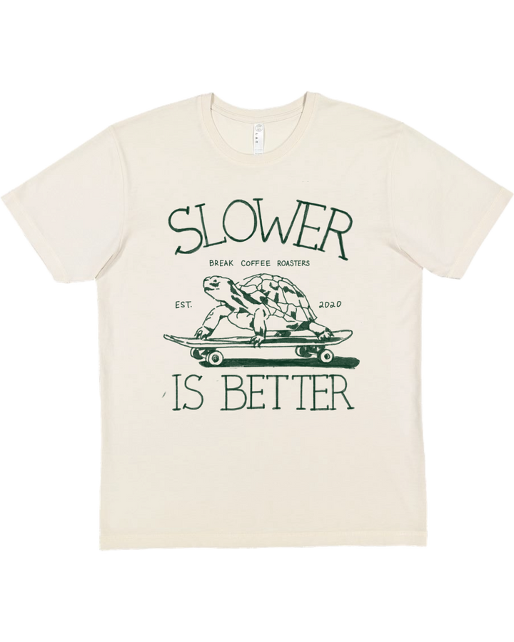 Beige t-shirt with a graphic of a turtle on a skateboard and text 'Slower is Better' on a white background.